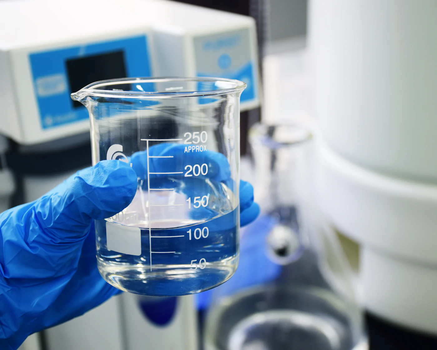 Lab technician in blue gloves holding a beaker of clear liquid